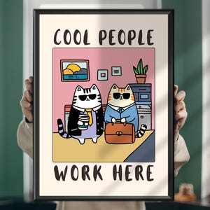 Peut inclure: Une affiche encadrée avec une illustration de dessin animé de deux chats en tenue de travail portant des lunettes de soleil. Le texte "COOL PEOPLE WORK HERE" est affiché au-dessus et en dessous de l'image. Les chats sont dans un bureau.