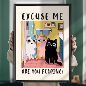 Op de afbeelding: Een ingelijste kunstprint met drie cartoonkatten in een badkamer. De katten, één wit, één oranje en één zwart, hebben grote ogen. De tekst "EXCUSE ME ARE YOU POOPING?" staat boven en onder de katten.
