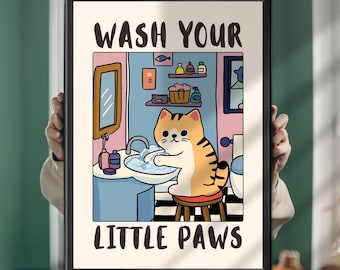 Könnte beinhalten: Ein gerahmter Kunstdruck mit einer Cartoon-Illustration einer orangefarbenen getigerten Katze, die ihre Pfoten in einem Waschbecken wäscht. Der Text WASH YOUR LITTLE PAWS ist oben und unten in Schwarz gedruckt. Die Szene zeigt einen Spiegel, Regale und Seife.