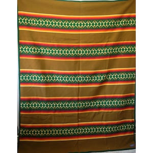 Puede incluir: Una manta marrón con bandas horizontales de patrones geométricos verdes intercaladas con rayas finas rojas, naranjas y amarillas. La manta tiene un borde verde oscuro sólido a lo largo de los lados y una textura textil uniforme.