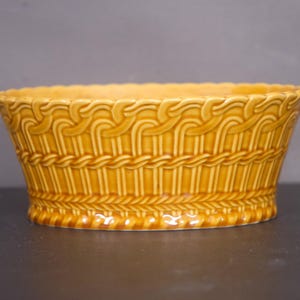 May include: A large, oval-shaped ceramic planter with a woven basket design. The planter is a light brown color.