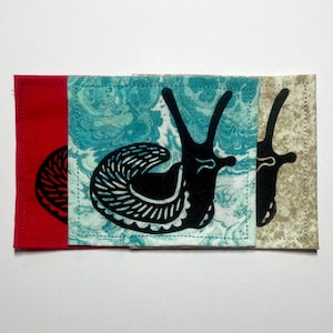 Peut inclure: Trois dessous de verre carrés en tissu avec une impression de silhouette d'escargot noir. Le dessous de verre de gauche est rouge uni, celui du centre présente un motif marbré turquoise et blanc, et celui de droite est beige et brun.
