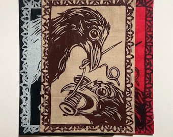 Puede incluir: Tres parches rectangulares de tela con un diseño serigrafiado de dos pájaros sosteniendo una aguja e hilo. El parche central es de color tostado con tinta marrón oscuro, el izquierdo es negro con tinta plateada y el derecho es rojo con tinta negra.
