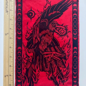 May include: Red and black rectangular patch featuring a raven with a sun in its beak, surrounded by flames. The design includes a border of crescent moons. The patch is approximately 25 cm long.