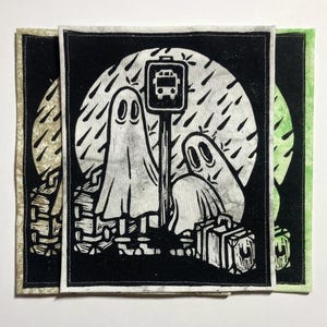 May include: Three square fabric patches with a black and white linocut print of two ghosts waiting at a bus stop in the rain. One ghost is standing, the other is sitting with a suitcase. The patches have different coloured borders.