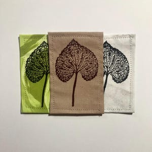 May include: Three rectangular fabric patches featuring a dark brown leaf print. The left patch is light green, the center patch is tan, and the right patch is off-white. Each patch has a stitched border and a single botanical leaf illustration.