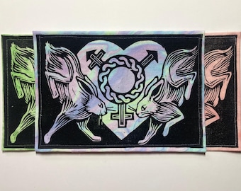 May include: Three rectangular fabric patches featuring a black background with a central heart shape containing a gender symbol. Two rabbits face each other on either side of the heart. The patches have iridescent, green, and pink color variations.