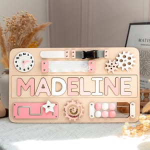 A wooden name board with the name "MADELINE" written on it, surrounded by various colorful and interactive elements such as gears, wheels, and a clock.