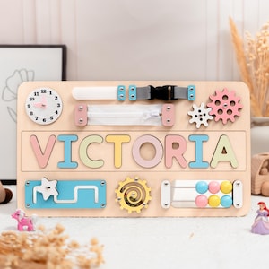 A wooden activity board with the name "VICTORIA" written on it, surrounded by various colorful and interactive elements such as gears, wheels, and a clock.