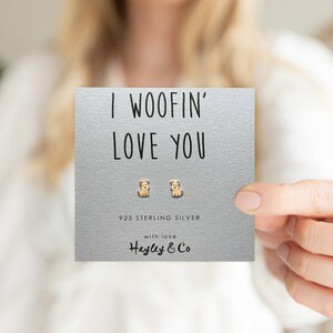 May include: A silver card with the text "I WOOFIN' LOVE YOU" and two small silver dog earrings. The card also says "925 Sterling Silver" and "with love Hayley & Co."