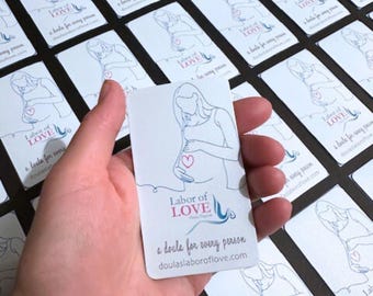 May include: A white card with a blue and pink illustration of a pregnant person holding their belly. The text on the card reads "Labor of Love Doula Program A doula for every person doulaslaboroflove.com"