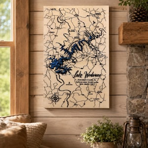 May include: A rectangular wooden wall art piece featuring a laser-engraved map of Lake Wedowee in Randolph County, AL. The map displays black road lines on a light wood background with the lake area in blue. Text includes Lake Wedowee, Surface area: 10,660 acres, Max. depth: 135 ft.
