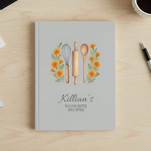 May include: A light gray cookbook with the text "Killian's Favourite Recipes". The cover features a watercolor illustration of a whisk, rolling pin, and spoon surrounded by orange flowers.