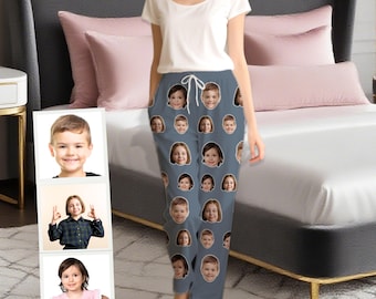 May include: Gray pajama pants featuring a repeating pattern of children's faces. The pants have a drawstring waist and are paired with a white scoop-neck t-shirt. The model is standing in a bedroom with a bed and pillows.