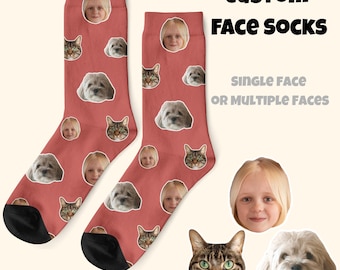 May include: A pair of custom face socks in a reddish-pink hue, featuring repeated images of a child, a cat, and a dog. The socks have black heels and toes. Text on the image reads "CUSTOM FACE SOCKS" and "SINGLE FACE OR MULTIPLE FACES."