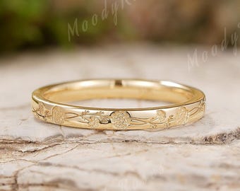May include: A gold band ring featuring a delicate, engraved floral pattern that wraps around the entire circumference of the metal surface. The ring has a polished finish and a slim, uniform width, showcasing intricate botanical details.