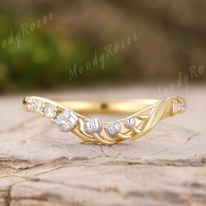 Op de afbeelding: Een goudkleurige ring met een bloemmotief, met kleine witte bloemen en heldere edelstenen. De ring heeft een gebogen vorm en is geplaatst op een getextureerd, lichtbruin oppervlak. De woorden "Moody Roses" zijn zichtbaar op de achtergrond.