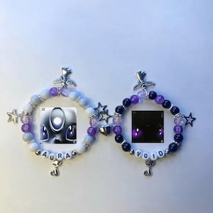 May include: Two beaded bracelets with the words "AURA" and "VOID". The bracelets feature white, purple, and black beads, with star and heart charms. Each bracelet has a cat charm and a small image.