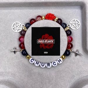 Puede incluir: Un brazalete de cuentas rojas, negras y doradas con un dije de pentagrama plateado, un dije de estrella plateada y cuentas de letras blancas que deletrean "CHURCH". El brazalete también tiene un dije de rosa roja y una pequeña portada de álbum con el texto "CHASE ATLANTIC" en él.