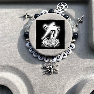 May include: A black and white bracelet with white beads that spell "GHOSTMANE" and black beads with silver skull charms. A silver pentagram charm hangs from the bracelet. A silver spider charm hangs from the bottom of the bracelet.