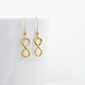 May include: A pair of gold infinity symbol earrings with a simple design. The earrings are on a white background.