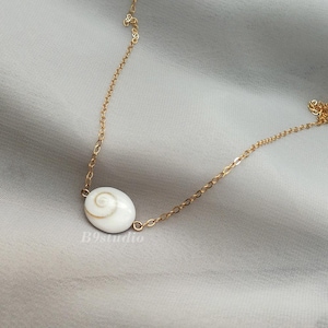 May include: A gold chain necklace with a white seashell pendant. The seashell has a spiral pattern.