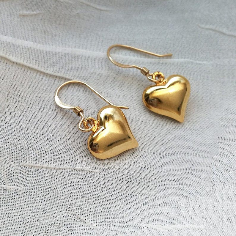 May include: A pair of gold heart-shaped dangle earrings. The earrings have a simple design and are made of a smooth, shiny metal.