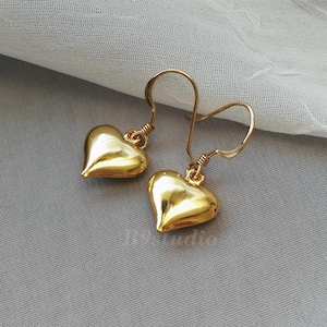 May include: A pair of gold heart-shaped dangle earrings with a simple wire hook closure.