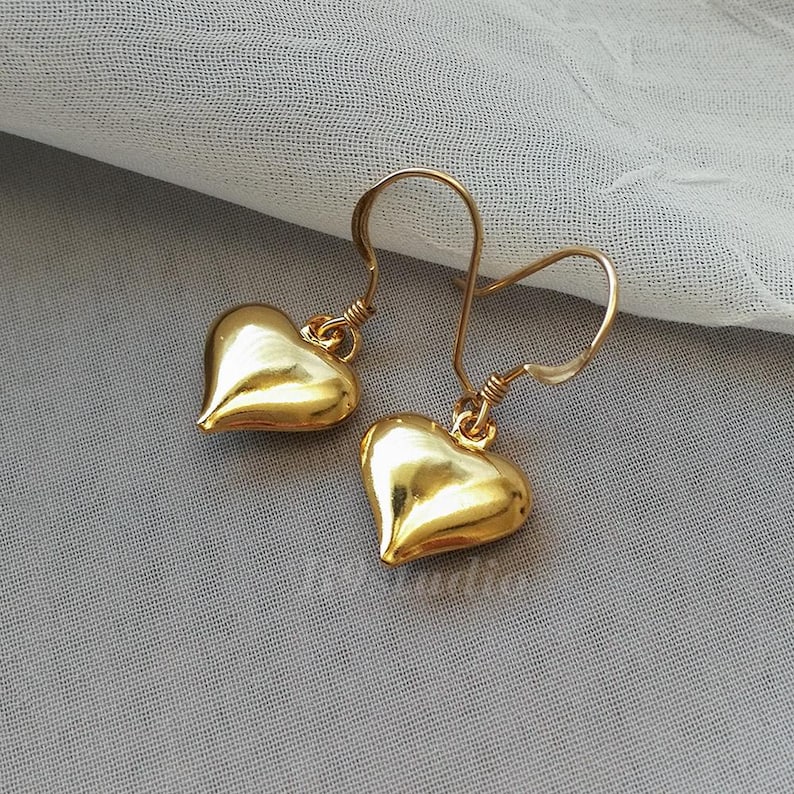 May include: A pair of gold heart-shaped dangle earrings with a simple wire hook closure.