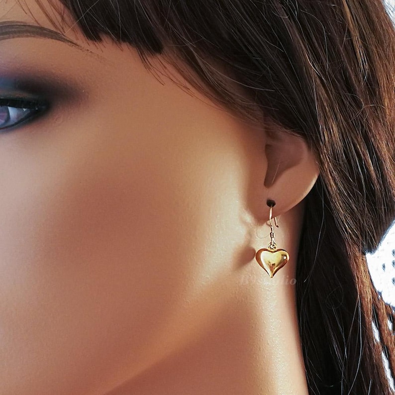 May include: Gold heart shaped dangle earrings. The earrings are small and delicate.