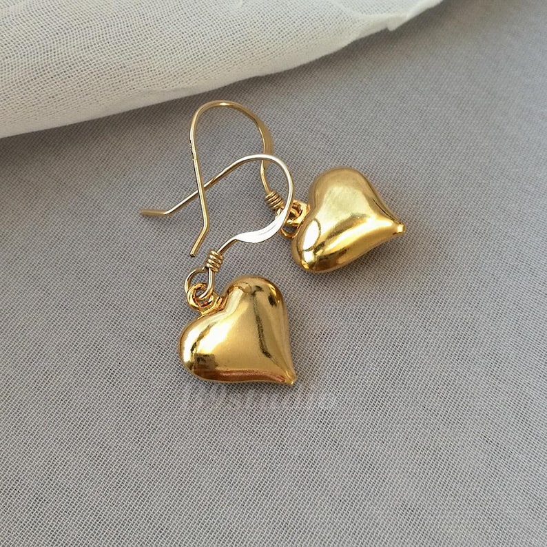 May include: A pair of gold heart-shaped earrings with a simple hook closure.
