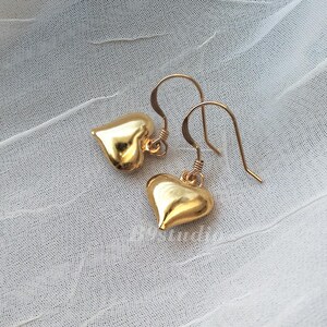 May include: A pair of gold heart-shaped dangle earrings with a simple hook closure.