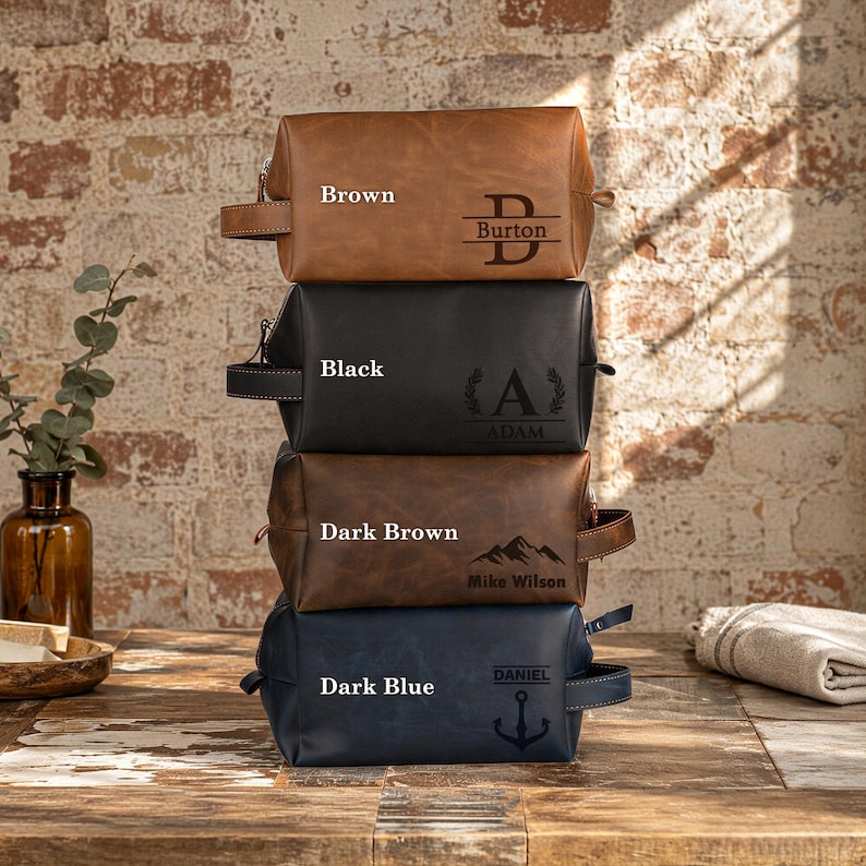 Puede incluir: Una pila de cuatro neceseres rectangulares en marr&oacute;n, negro, marr&oacute;n oscuro y azul oscuro. Cada bolsa cuenta con un asa lateral, cierre de cremallera y grabados personalizados que incluyen los nombres Burton, Adam, Mike Wilson y Daniel.