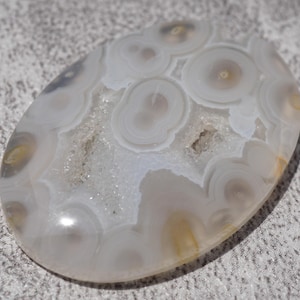 May include: A white agate cabochon with a unique pattern of concentric circles and swirls. The stone has a smooth, polished surface and a natural, organic shape.