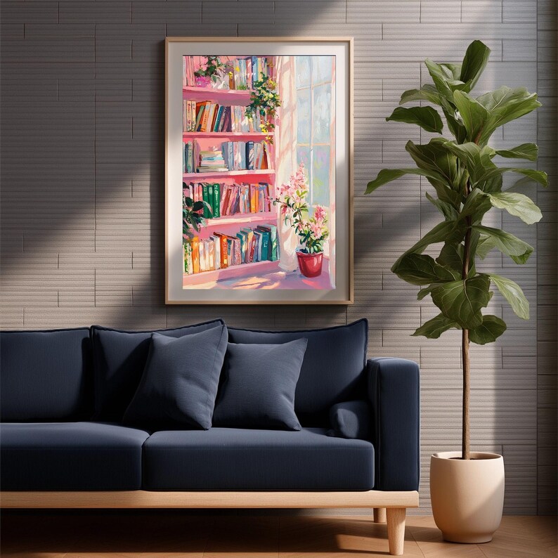 K&ouml;nnte beinhalten: Ein gerahmtes Kunstwerk zeigt ein rosa B&uuml;cherregal voller B&uuml;cher und Pflanzen, das von Sonnenlicht von einem Fenster beleuchtet wird. Unter dem Kunstwerk befindet sich ein marineblaues Sofa mit Kissen, und rechts steht eine Topfpflanze.