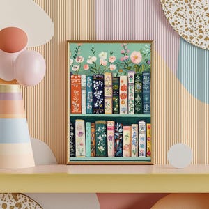 May include: A framed art print featuring a bookshelf filled with colorful books. The books have floral designs and are arranged on two shelves. The background is a soft green with flowers at the top. The frame is gold.