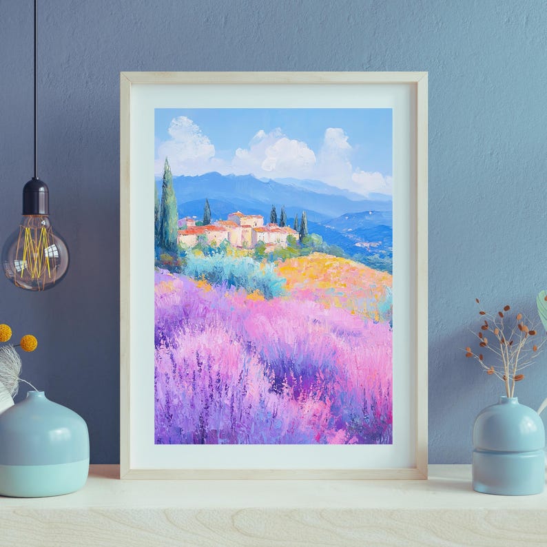 May include: A framed painting of a landscape with a small village nestled in a field of purple lavender flowers. The village is surrounded by rolling hills and a blue sky with white clouds.