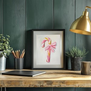 May include: A framed painting of a pink and gold candy cane with a pink bow on a white background.