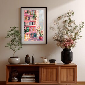 K&ouml;nnte beinhalten: Ein gerahmtes Gem&auml;lde zeigt ein rosa B&uuml;cherregal mit bunten B&uuml;chern, Pflanzen und Sonnenlicht, das durch ein Fenster scheint. Es h&auml;ngt &uuml;ber einem Holzschrank mit Dekorationen und einer Topfpflanze.