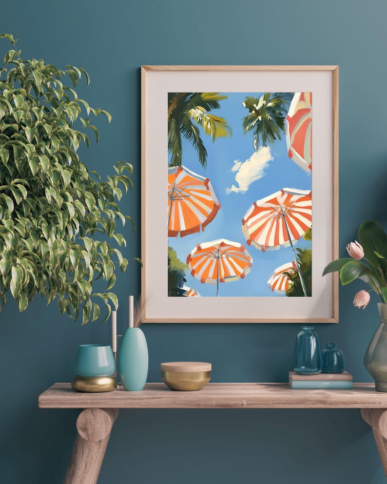 May include: A framed painting of a summer scene with orange and white striped beach umbrellas against a blue sky with palm trees.