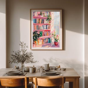 K&ouml;nnte beinhalten: Ein gerahmtes Gem&auml;lde zeigt ein rosa B&uuml;cherregal voller bunter B&uuml;cher, Pflanzen und Sonnenlicht, das durch ein Fenster scheint. Das Kunstwerk wird &uuml;ber einem Holzesstisch mit Tellern, Tassen und einer Vase mit Gr&uuml;nzeug ausgestellt.