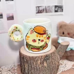 手描きの猫が描かれた陶器のマグカップ、ハンバーガー型の取っ手が付いた陶器のティーカップ、手作りの陶器のコーヒーカップ、ティーカップ