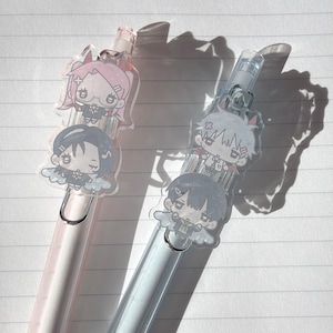 May include: Two pens with anime-style character charms. One pen is light pink, the other is light blue. Each pen has two charms with different characters. The charms are clear with black and pastel color details.