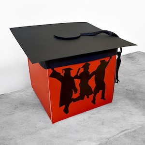 May include: A red box shaped like a graduation cap with three black silhouettes of graduates raising their arms in celebration. The box has a black tassel.
