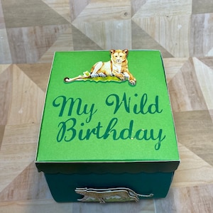 May include: A green box with the text "My Wild Birthday" in a script font. The box is decorated with a lion and a cheetah. The box is a dark green color.