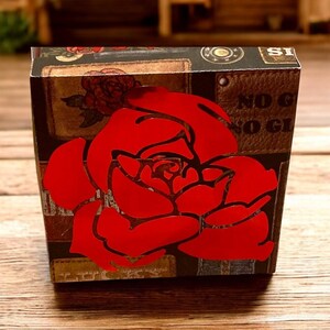 May include: A small, square gift box with a large red rose design on the front. The box has a brown background with a collage of vintage-style images. The words "NO G" are visible on the side.