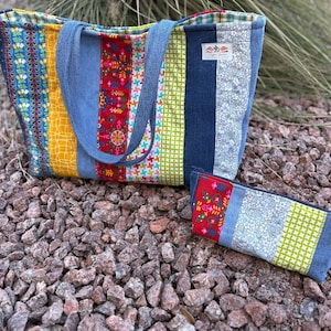 May include: A patchwork tote bag and matching pencil case. The tote bag has blue denim handles and is made of colorful fabric strips in yellow, red, blue, and green. The pencil case mirrors the bag's design, featuring similar fabric patterns.
