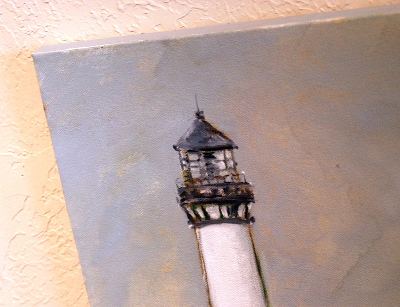 May include: A close-up of a white lighthouse with a black and gray roof and a black railing. The lighthouse is painted against a light blue sky.