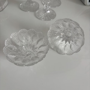 May include: Two clear glass candle holders with a decorative floral pattern. The candle holders have a wide base and a narrow top.