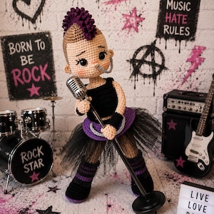May include: A crocheted punk rock doll with a purple mohawk, holding a microphone. The doll is dressed in a black top, a purple and black tutu, and striped leg warmers. The background includes graffiti art and the words "Punk," "Love Music Hate Rules," and "Born to be Rock."